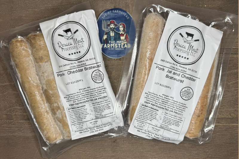 Two packages of Pork Cheddar Bratwurst and Pork Jalapeno Cheddar Bratwurst with The MF'n Farm labels on a wooden surface.