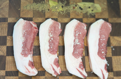 Pasture-raised Meishan heritage pork chops from The MF Farmstead in Carrollton, Georgia, seasoned with coarse salt and herbs on a wooden board.