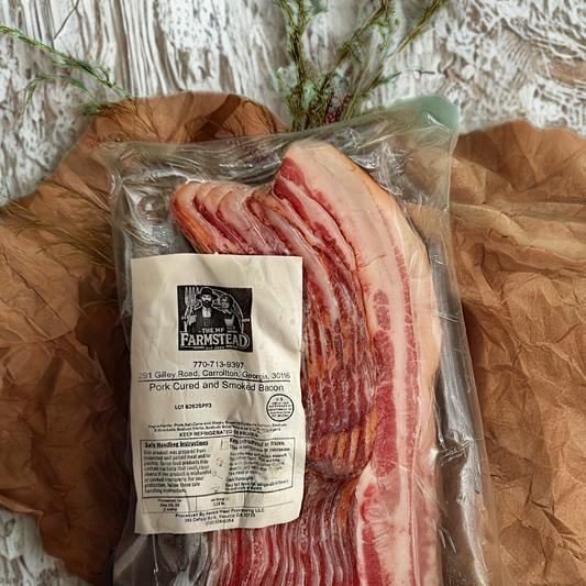A vacuum-sealed package of bacon strips laid on brown paper with decorative greenery. The front label reads 'The Farmstead' and 'Pork Cured and Smoked Bacon'.
